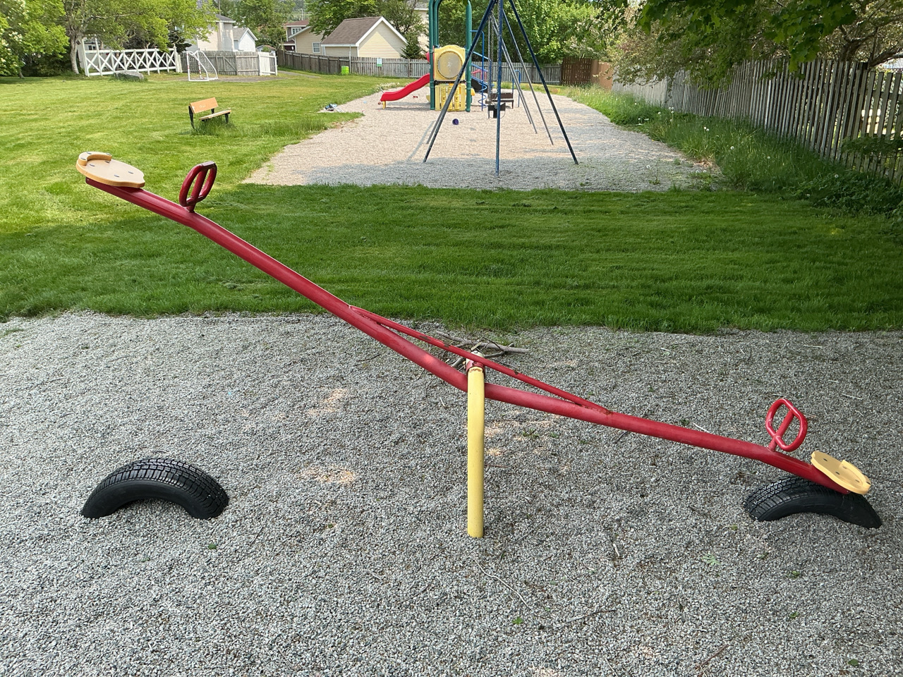 teeter-totter with playground equipment int he background 